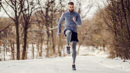 Junger Sportler läuft im Wald auf einem schneebedeckten Weg. Junger Sportler läuft im Wald auf einem schneebedeckten Weg.