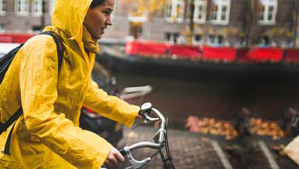 Frau in gelbem Regenmantel fährt mit dem Fahrrad durch Amsterdam. Frau in gelbem Regenmantel fährt mit dem Fahrrad durch Amsterdam.