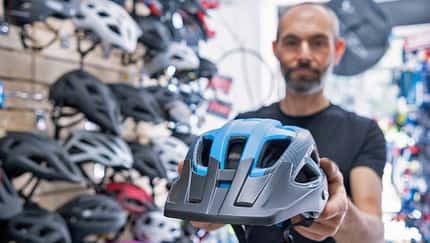 Verkäufer im Radladen steht vor einer Wand mit Helmen und präsentiert einen blauen Helm. Verkäufer im Radladen steht vor einer Wand mit Helmen und präsentiert einen blauen Helm.