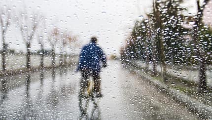 Durch Regentropfen verschwommenes Bild eines Radfahrers mit blauem Regencape. 