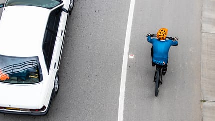 Ein weißes Auto überholt einen Fahrradfahrer. Ein weißes Auto überholt einen Fahrradfahrer.