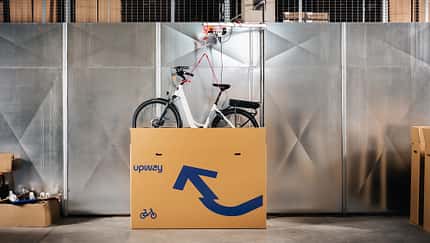 Ein Fahrrad wird aus einem Karton mit Upway-Schriftzug gehoben. 