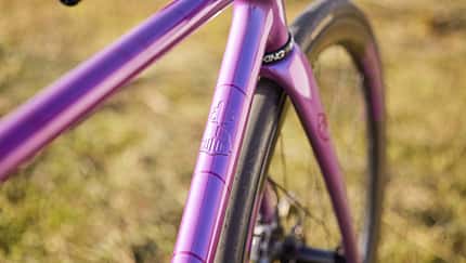Detailaufnahme des lilafarbenen Fahrradrahmens eines IRIS x St Joris Modells, Fokus auf Steuerrohr und Branding.