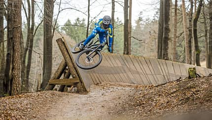 Mountainbiker auf einem Trail im Bikepark Beerfelden, fährt auf einer Holzkurve (Wallride) durch den Wald.