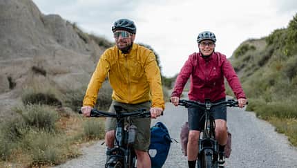 Zwei Radfahrer in bergiger Umgebung mit Regenkleidung. 