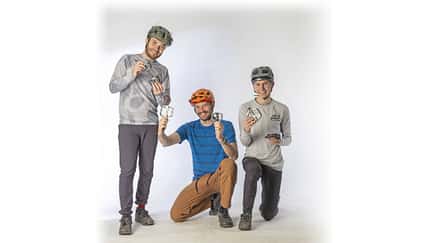 Drei Männer mit Fahrradhelmen präsentieren verschiedene Fahrradpedale im Studio vor weißem Hintergrund.