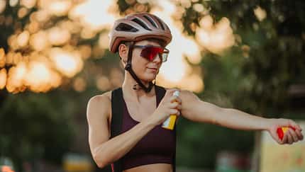Cyclist applying sunscreen or mosquito repellent before cycling outdoors Cyclist applying sunscreen or mosquito repellent before cycling outdoors