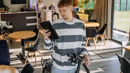 Mann, der sich im Café um sein Elektrobike kümmert und mit seinem Tablet nach etwas sucht. Mann, der sich im Café um sein Elektrobike kümmert und mit seinem Tablet nach etwas sucht.