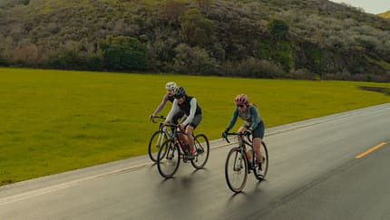 Drei Rennradfahrer:innen auf Straße,Hügel Drei Rennradfahrer:innen auf Straße,Hügel