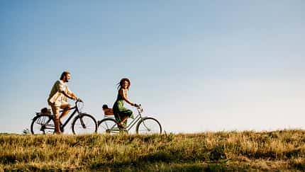Ein Mann und eine Frau auf Fahrrädern auf einer Wiese vor blauem Himmel. Ein Mann und eine Frau auf Fahrrädern auf einer Wiese vor blauem Himmel.