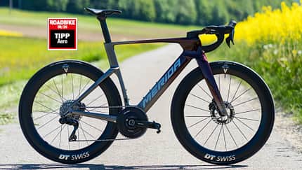 Das Merida Reacto One mit Roadbike Testsiegel "Tipp Aero" in seiner rot-grauen Lackierung auf einer asphaltierten Straße. Das Merida Reacto One mit Roadbike Testsiegel "Tipp Aero" in seiner rot-grauen Lackierung auf einer asphaltierten Straße.