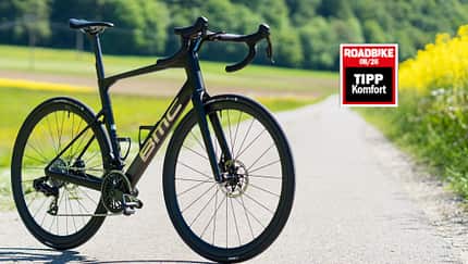 Die BMC Roadmachine 01 Two in seitlicher Ansicht von vorne auf einem asphaltierten Weg in schwarzer Lackierung. Die BMC Roadmachine 01 Two in seitlicher Ansicht von vorne auf einem asphaltierten Weg in schwarzer Lackierung.