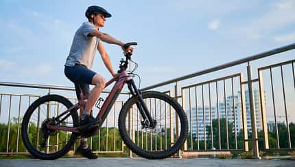Mann fährt E-Bike auf der Stadtpromenade, Seitenansicht Radfahrer gegen blauen Himmel. Mann fährt E-Bike auf der Stadtpromenade, Seitenansicht Radfahrer gegen blauen Himmel.