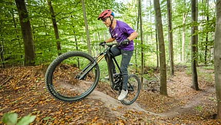 Schorndorf, E-Mountainbike, Mountainbike, Mittelmotor, Federgabel, Singletrail, Bergauffahrt, Waldweg, Fahrradsport, E-Mobilität Das Foto zeigt einen Fahrer auf einem Mountainbike auf einem Wald‑Singletrail bei Schorndorf, aufgenommen am 15.09.2026 laut Dateiname. Das Rad ist als E‑Mountainbike mit Mittelmotor und integriertem Akku im Unterrohr erkennbar; eine lange Federgabel und grobstollige Reifen unterstützen die Bergauffahrt.