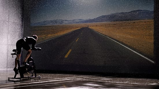 Man using exercise bike in front of road on screen, rear view