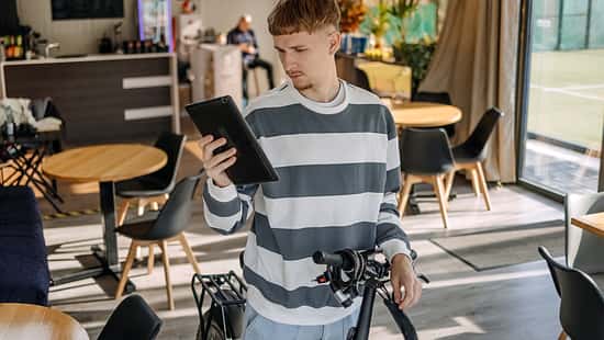 Mann, der sich im Café um sein Elektrobike kümmert und mit seinem Tablet nach etwas sucht.
