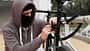 Caucasian male Thief in balaclava and hood breaks the lock on a bicycle in the street during the day. Closed face and hacking. Stealing bicycles.