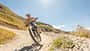 Mountainbiker fährt dynamisch auf Schotterweg durch sonnige Hügellandschaft
