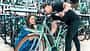 Verkäufer erklärt einer Kundin die Funktionen eines E-Bikes in einem Fahrradladen, beide lächeln und beugen sich zum Rad.