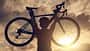 Rear view of cyclist woman lifting her bicycle above her head after finished her exercise workout during sunset.