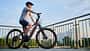Mann fährt E-Bike auf der Stadtpromenade, Seitenansicht Radfahrer gegen blauen Himmel. 