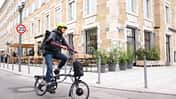 City E-Bike I Test E-Faltrad Brompton Electric P-Line Urban I Frau auf Brompton Faltrad in der Stadt City E-Bike I Test E-Faltrad Brompton Electric P-Line Urban I Frau auf Brompton Faltrad in der Stadt