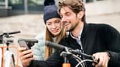 Smiling couple with bicycles and cell phone in the city