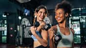 Latino and African sport woman exercising and build muscle in stadium. Active strong beautiful fit athlete girls in sportswear workout lifting weight dumbbell for arm and health care at fitness club.
