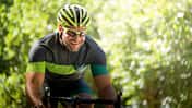 Smiling young man riding bicycle against trees