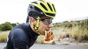 Man eating pizza while cycling on street against clear sky