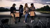 Vier Freunde essen Pizza auf einer Brücke bei Sonnenuntergang, mit Fahrrädern im Vordergrund. Vier Freunde essen Pizza auf einer Brücke bei Sonnenuntergang, mit Fahrrädern im Vordergrund.