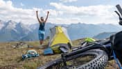 Woman bikepacking and camping, she set up her tent on top of the mountains, arms up