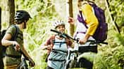 Smiling friends in discussion while resting during mountain bike ride in forest