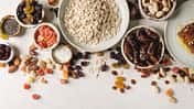 Variety of dried fruits. nuts. honey and oat flakes in ceramic bowls for cooking homemade healthy breakfast muesli or granola energy bars over white texture background. Flat lay. space.