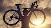 Rear view of cyclist woman lifting her bicycle above her head after finished her exercise workout during sunset.