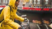 Frau in gelbem Regenmantel fährt mit dem Fahrrad durch Amsterdam.