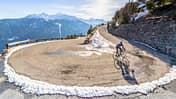 Road cyclist climbing hairpin bends up mountain pass in winter with snow.