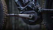 Detailaufnahme eines E-Bike-Mittelmotors mit Kurbel und Pedal, montiert an einem Mountainbike-Rahmen.