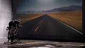Man using exercise bike in front of road on screen, rear view