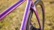 Detailaufnahme des lilafarbenen Fahrradrahmens eines IRIS x St Joris Modells, Fokus auf Steuerrohr und Branding.