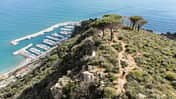Luftaufnahme eines Küstenhügels mit Mountainbiker auf einem Trail, darunter ein Yachthafen am Meer.