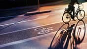 Radweg am Abend. Schild für Fahrrad auf den Asphalt gemalt. Auto und Verkehr im Hintergrund. 