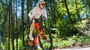 Frontalansicht einer Radsportlerin auf dem orangenen Storck Fascenario.5 in Fahrt auf einer Landstraße im Wald.